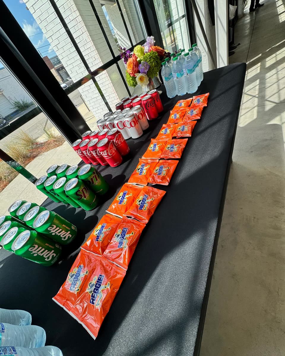 Dozens of REGGIE! Bars laid out in a long row on a black event table beside cans of soda