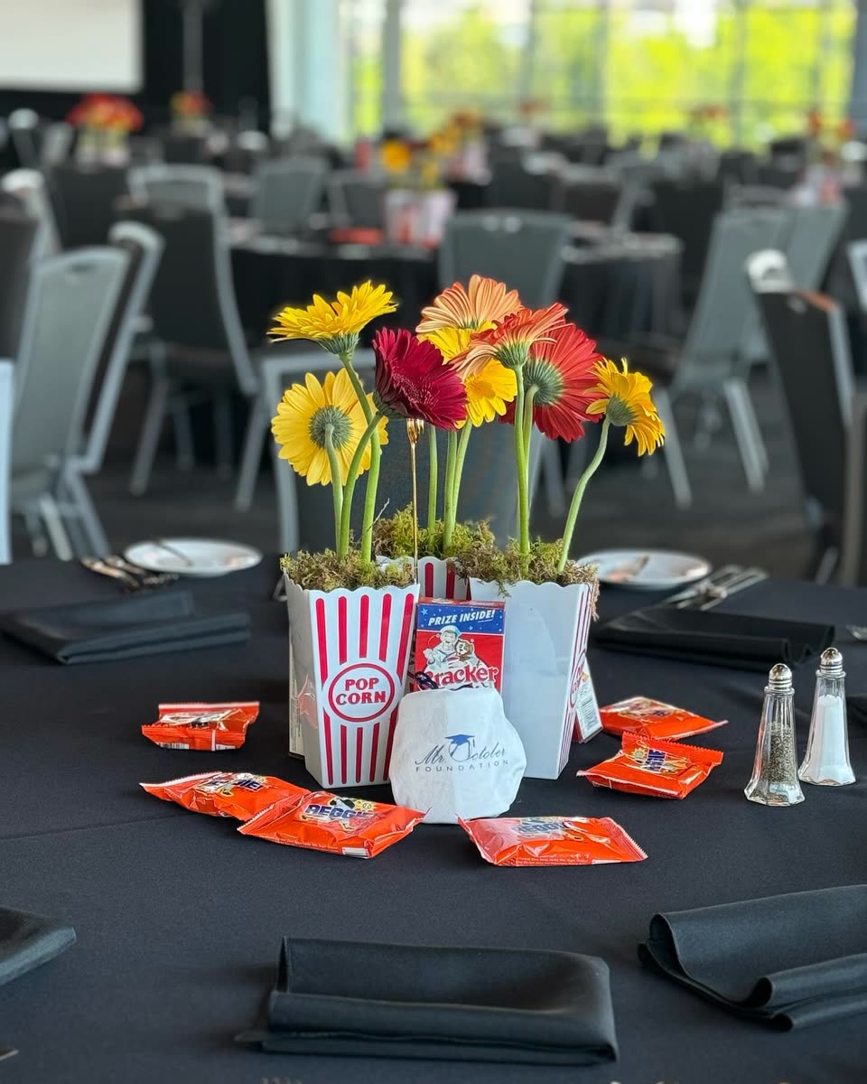 A ballpark-themed centerpiece of popcorn cups and flowers with REGGIE! Bars scattered across the tablecloth