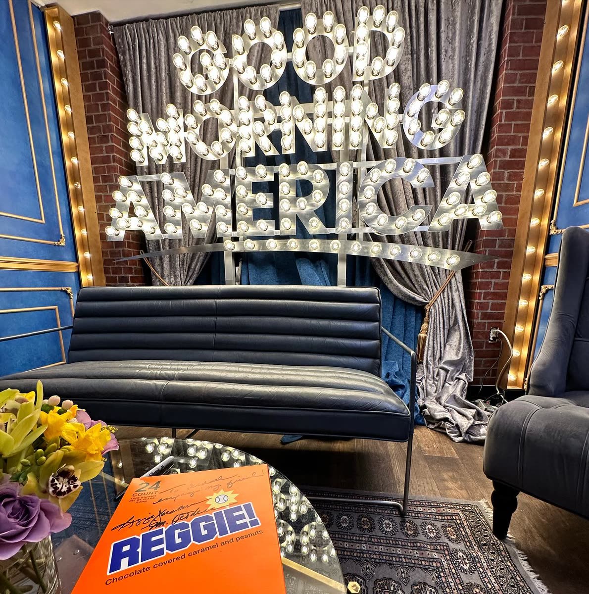 A signed 24-count REGGIE! box resting on a table in front of the lit Good Morning America marquee sign