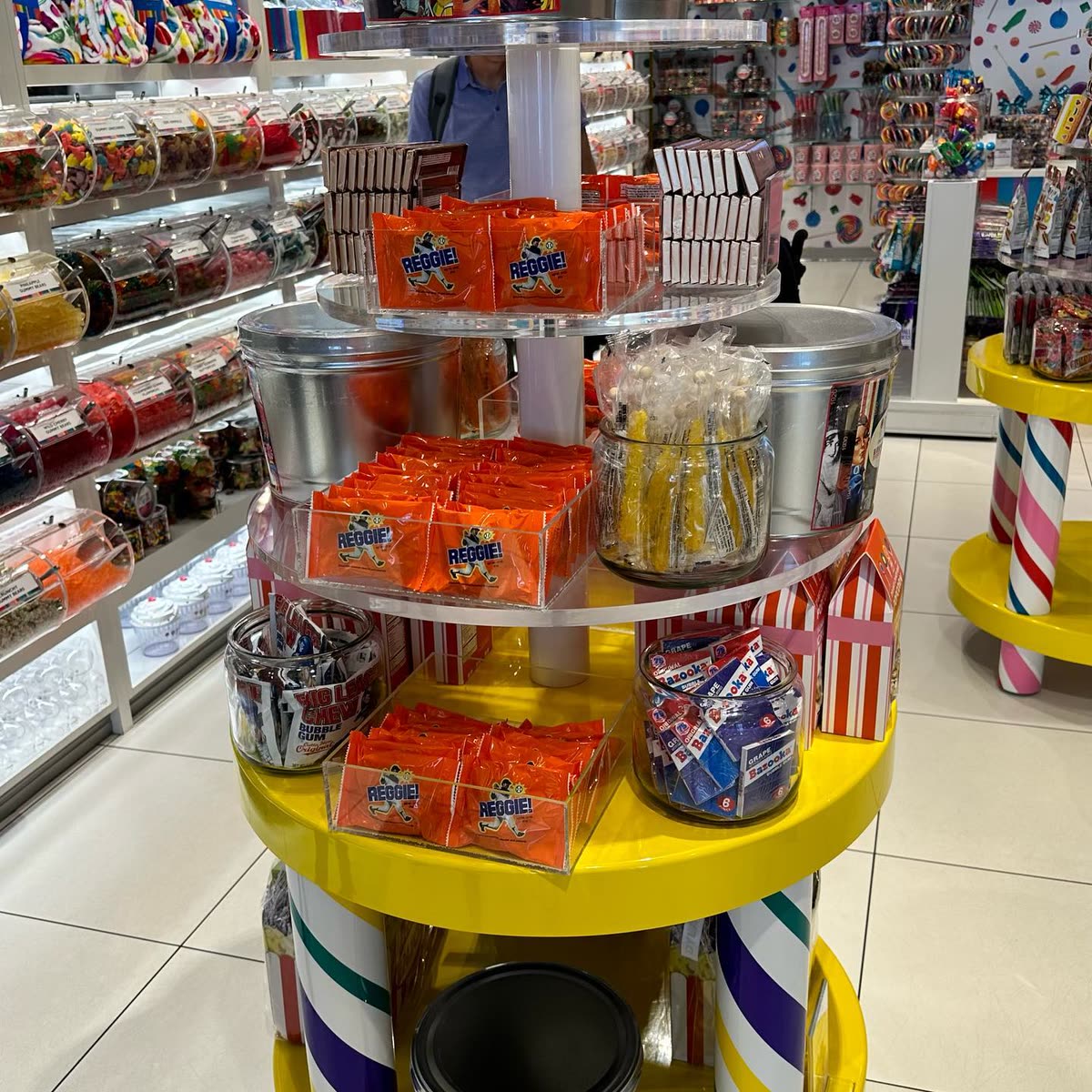 A tiered candy store display tower filled with trays of orange REGGIE! Bars