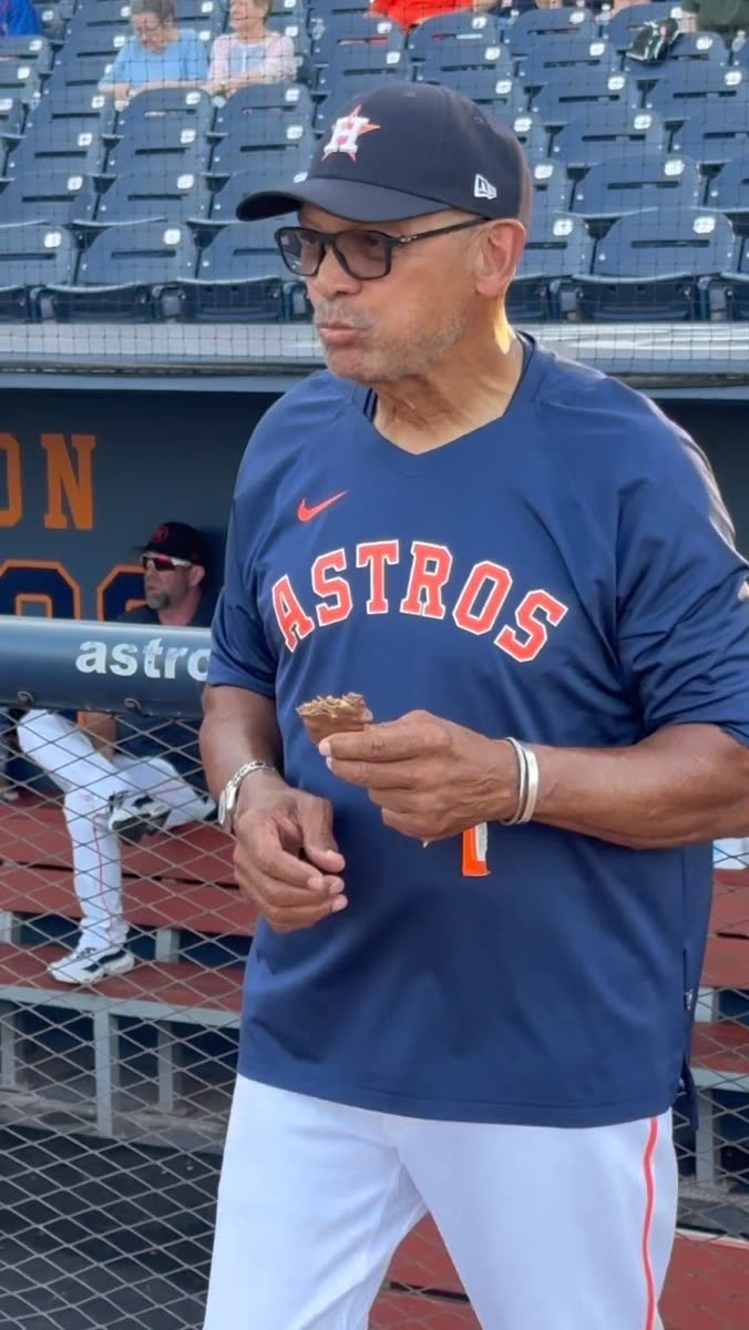 Reggie Jackson in a baseball jersey eating a REGGIE! Bar beside the dugout