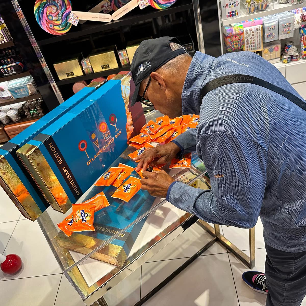 Reggie Jackson bending over a display case to sign individual REGGIE! Bar wrappers with a marker