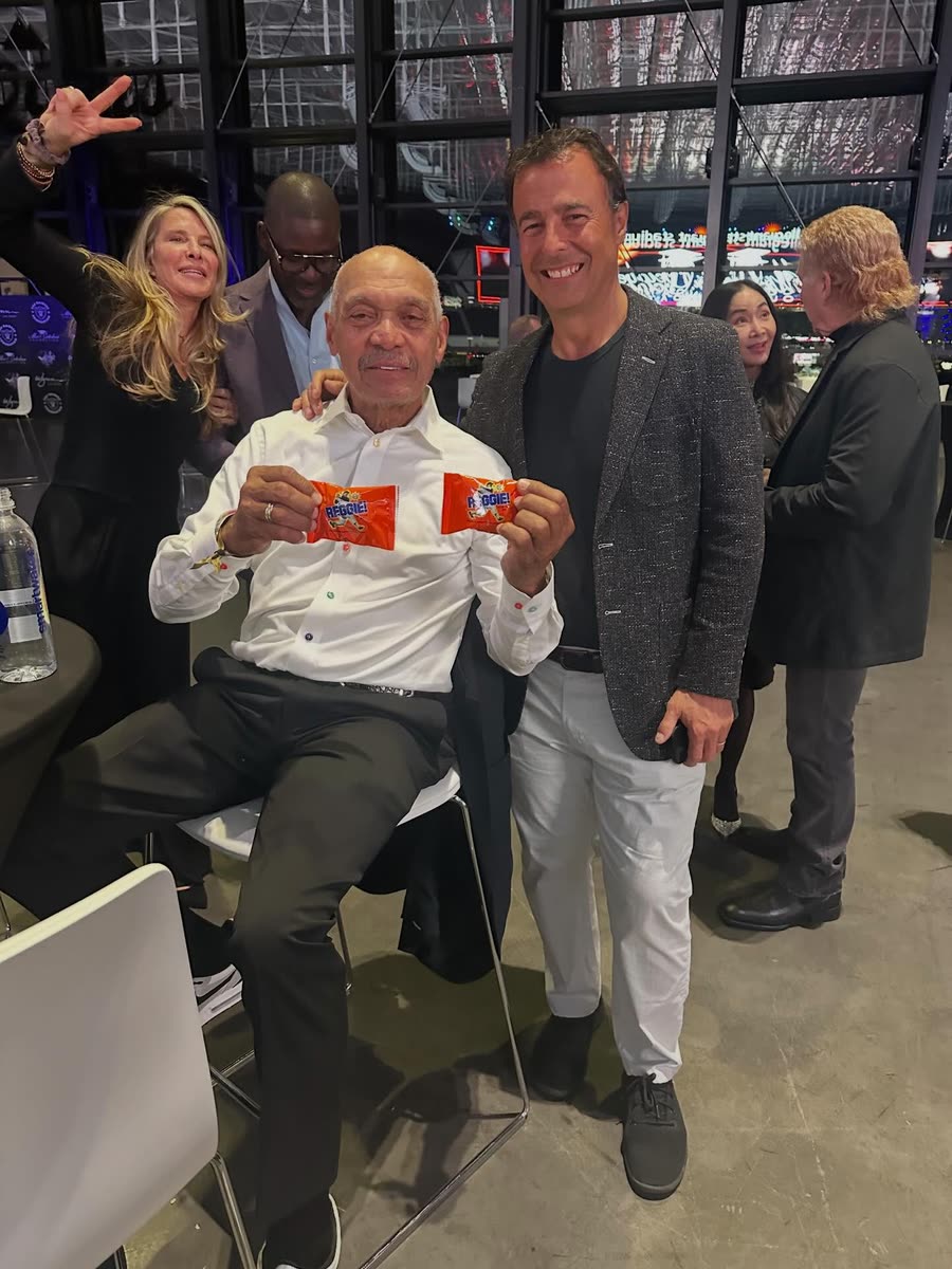 Reggie Jackson seated at an event holding up two REGGIE! Bars, one in each hand